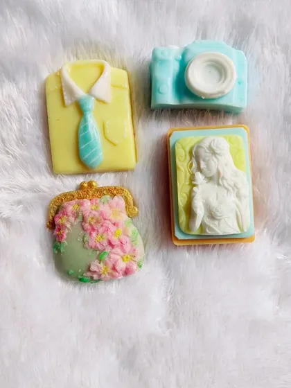 A set of four different themed soaps: a shirt and tie, a camera, a floral purse, and a cameo.