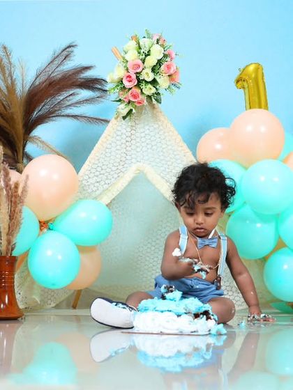 A baby boy gets ready to smash his cake in a cute setup with a teepee and pastel balloons. The "ONE" blocks and teddy bear add a classic touch to this first birthday shoot.