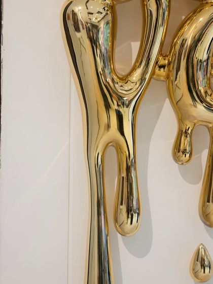 A detail of the dripping golden forms in the "Love Drip" sculpture, their fluid shapes conveying a sense of abundant emotion.