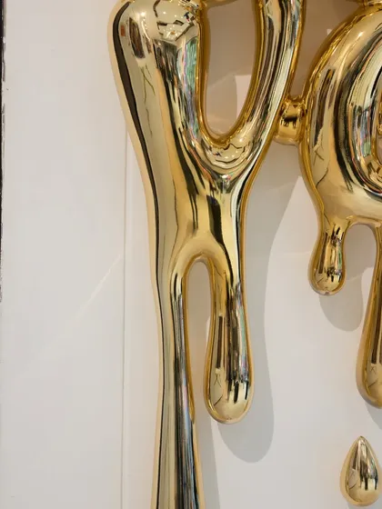 A detail of the dripping golden forms in the "Love Drip" sculpture, their fluid shapes conveying a sense of abundant emotion.