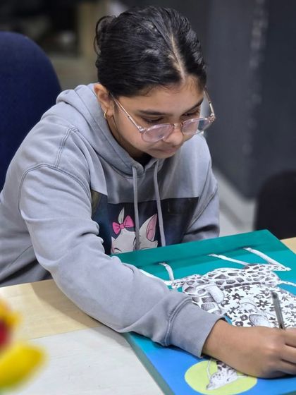A young student fully concentrated on her creative artwork, demonstrating the focus and skill she has developed in our classes.