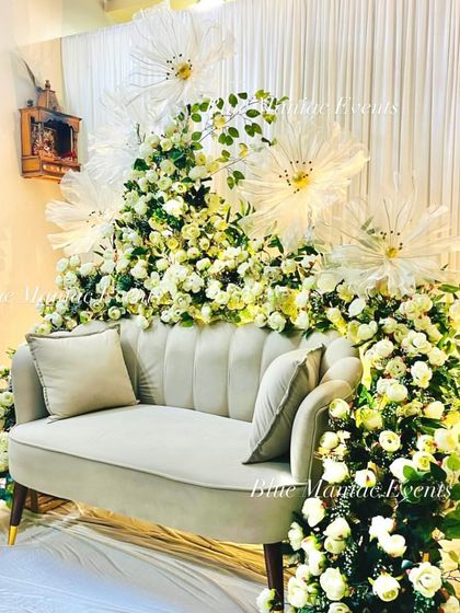 This image shows the full engagement setup with the unique floral arrangement enveloping the loveseat. It creates a stunning, immersive photo booth that feels like sitting in a cloud of flowers.