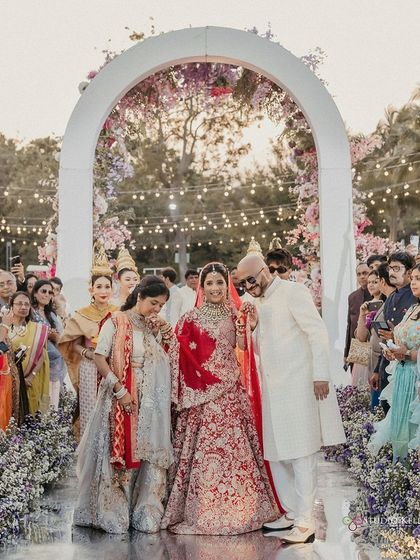 The bride's emotional and beautiful entrance with her parents, walking down a flower-lined aisle at her Thailand wedding.