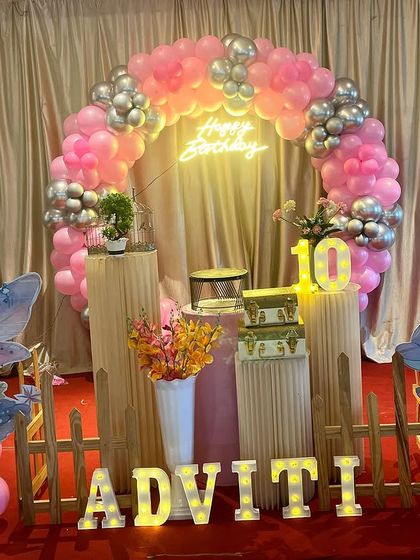 A combined fairy and mermaid theme for a 10th birthday. This stage setup includes a pink and silver balloon ring, character cutouts, and marquee letters for the name.