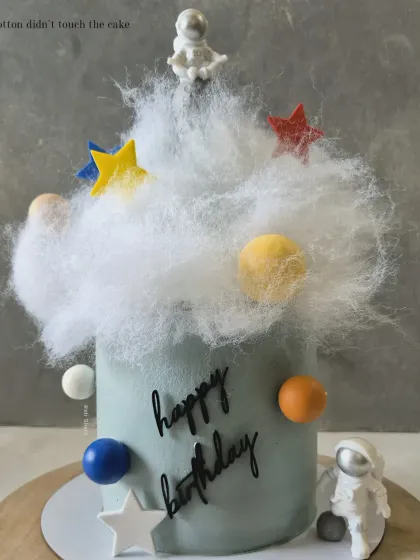 An out-of-this-world space-themed cake with an astronaut, planets, and stars, using cotton candy for a fluffy cloud effect.