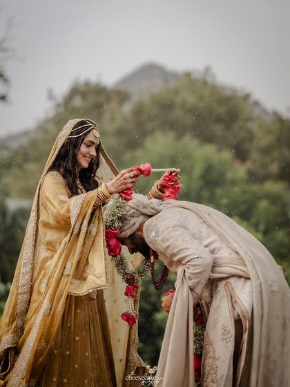 A playful and triumphant moment during the Varmala, as the bride garlands the groom under a shower of rain and petals.