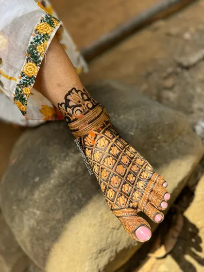A unique shot of a bridal leg design resting on a rock, showcasing the beautiful contrast of the henna against a natural element.