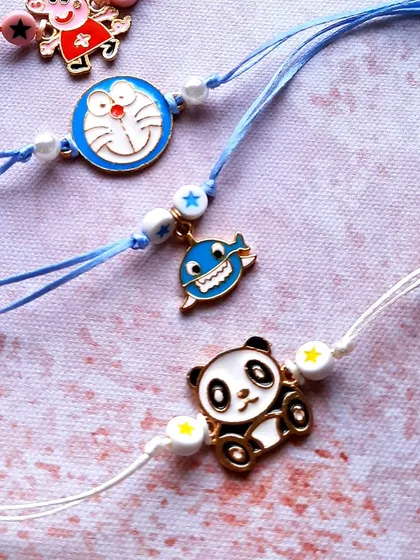 More character fun. This image shows a cute panda and a happy whale charm, perfect for kids who love animals. The Doraemon and Peppa Pig Rakhis are also part of this collection.