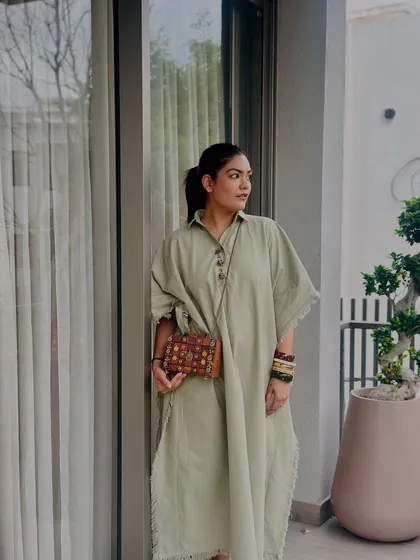 A candid shot showing the wooden clutch as part of a relaxed, elegant outfit. The natural wood tones are a perfect complement to the earthy green of the dress.