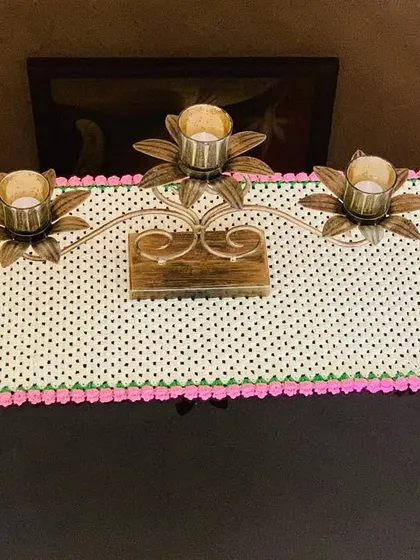This simple yet beautiful table runner features a cream-colored granny stitch pattern with a bright pink tulip border. It's shown here on a console table with a candle stand.