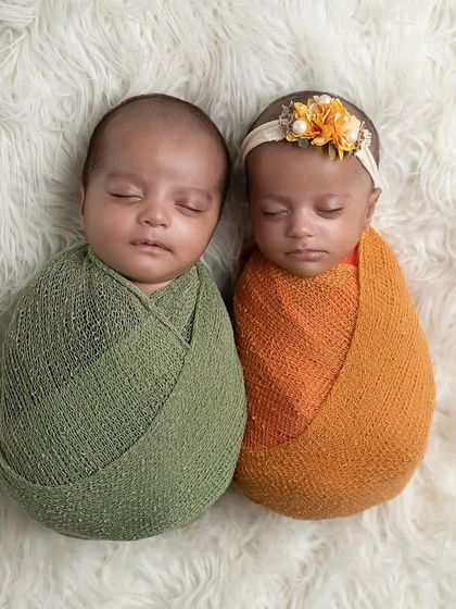 A sweet shot of newborn twins, swaddled in complementary colors, nestled together on a soft white rug.