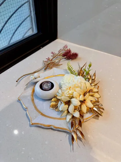 This handcrafted coin tray is designed to hold shagun with grace. The marble-finish platter is decorated with artificial flowers and includes a small, ornate container for the coin or roli-chawal.
