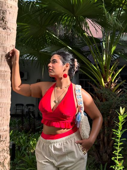 Waiting for life to sound like a Bad Bunny song again. A golden hour shot in a red bikini top and linen pants, surrounded by palm trees.