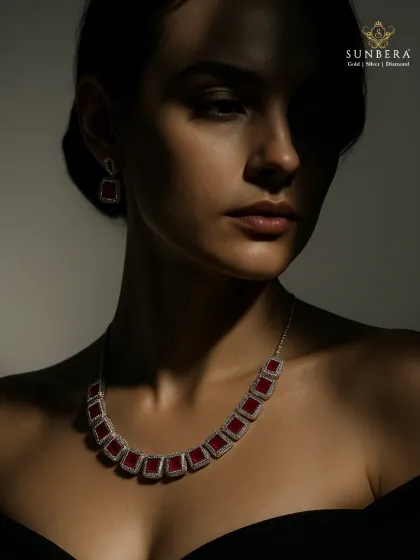 A model wears the ruby and diamond necklace, showcasing how the piece sits elegantly on the neckline. The play of light and shadow highlights the dramatic contrast and luxurious feel of the jewellery.