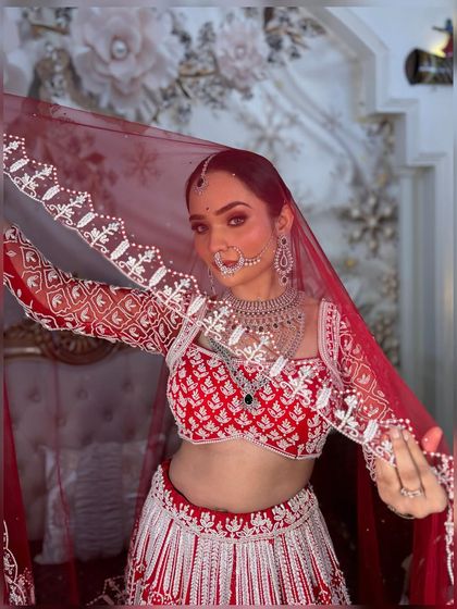 The classic bridal veil shot. The sheer red dupatta beautifully frames her face, highlighting the intricate makeup and jewellery.
