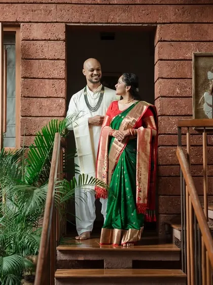 A candid moment of shared admiration between the couple on the stairs of a modern home with traditional touches, showcasing their elegant ethnic wear.
