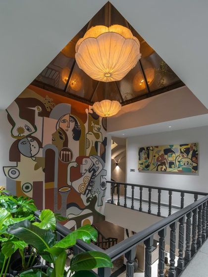The interplay of light, architecture, and art. The skylight and pendant lamps cast a warm glow on the mural, highlighting its colors and forms and creating a dynamic, inviting atmosphere.