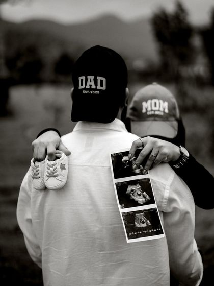 A fun and modern announcement from behind. The couple wears "Mom" and "Dad" caps, and she holds up baby shoes and the sonogram. It's full of personality.