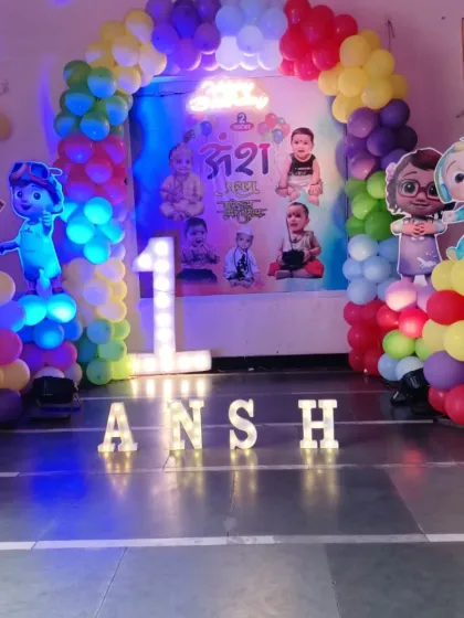 This is a closer look at a Cocomelon first birthday party setup. It features a custom backdrop with the baby's photos, character cutouts of JJ and his friends, and marquee lights spelling out the birthday boy's name.