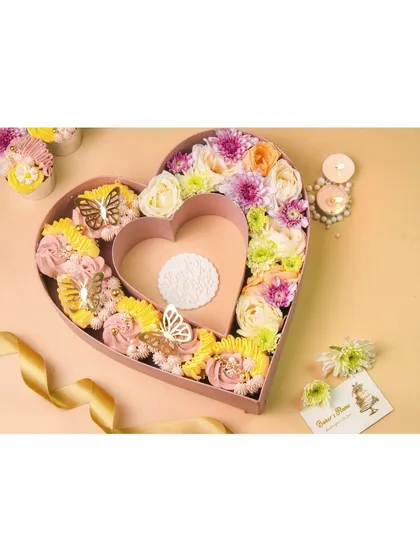 A large, heart-shaped gift box filled with decorated cupcakes and fresh flowers, an ideal shot for a premium bakery.