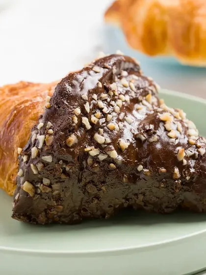 A chocolate croissant on a pastel green plate. The simple composition and soft lighting make this a very elegant and appealing shot for a bakery.