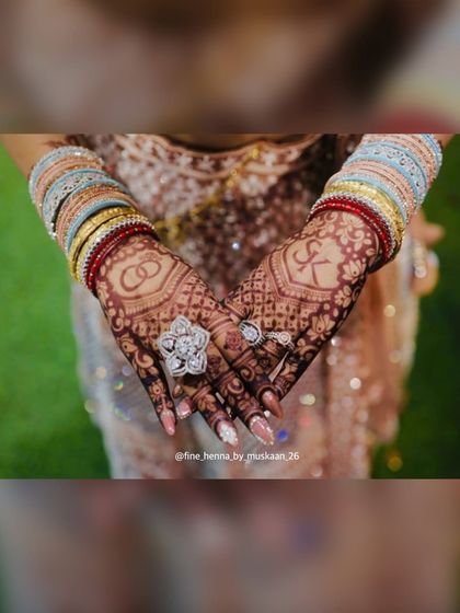 The final look of this engagement mehndi, complete with bangles and rings. The design features interlocking rings and the initial 'K'.
