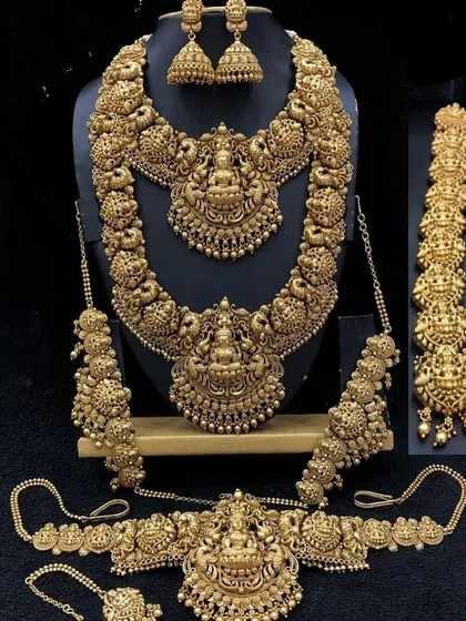 This is a full antique-finish temple jewellery set, perfect for achieving a classic bridal look. The set includes a choker, a long haaram, matching jhumkas, a vaddanam (waist belt), and hair accessories, all featuring intricate deity and peacock motifs.