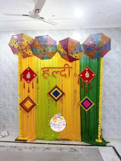 A vibrant Haldi ceremony backdrop with yellow and green drapes, decorated with colorful umbrellas and traditional hangings.