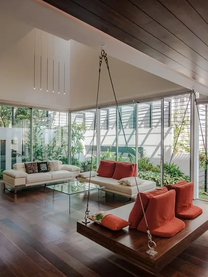 a wide perspective of the suspended wooden swing, designed as the centerpiece of a modern family living space with floor-to-ceiling glass walls…