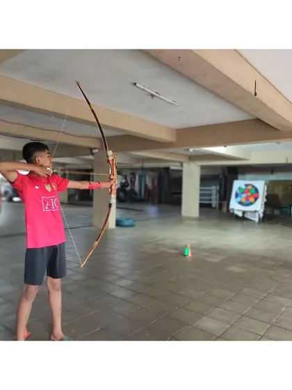 A young archer in the middle of his draw, focusing intently on the target. Practice like this builds muscle memory and discipline.
