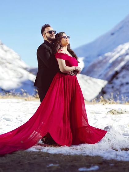 A dramatic pose against a snowy mountain backdrop. The contrast between the hot pink-red gown and the white snow is absolutely breathtaking.