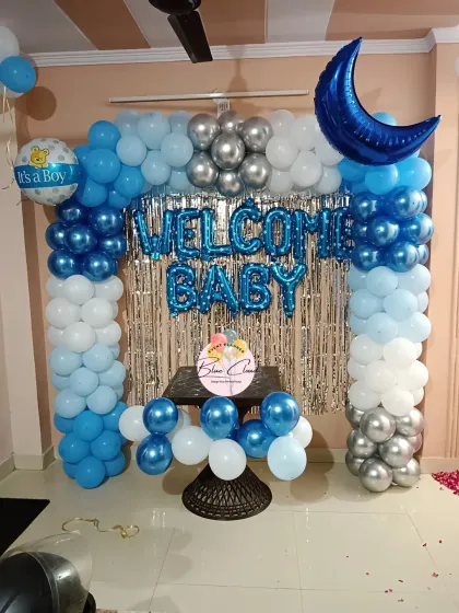 A 'Welcome Baby' boy decoration with a blue, white, and silver balloon arch and a shimmer curtain.