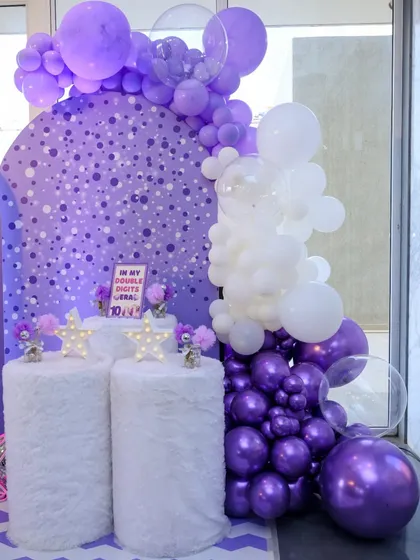 The cake display area for the lavender party, featuring fluffy white pedestals, star lights, and a backdrop of purple and white balloons.