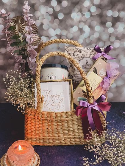 Another view of the sustainable "Tyohaar" basket, highlighting the handmade quality and the elegant arrangement of snacks, flowers, and a lit candle against a festive backdrop.