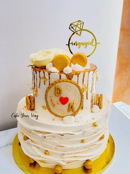 Dripping in gold and love. A two-tier engagement cake with a gold drip, ruffles, and macarons.