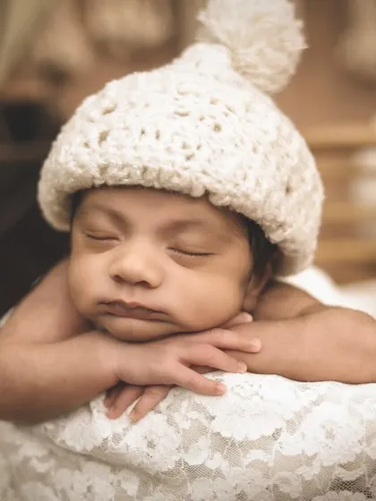 A sweet close-up of a newborn with a cozy knit pom-pom hat, resting his chin on his hands. The soft lace and simple hat keep the focus on the baby's adorable face.