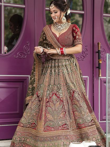 A full shot of a heavily embroidered bridal lehenga in shades of maroon and olive green. This is a unique color combination for the bride who wants to stand out.