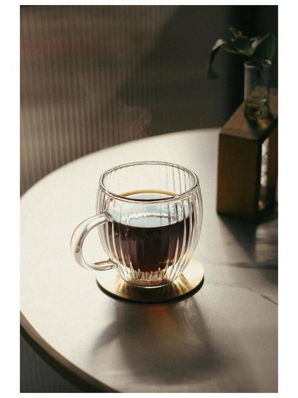A beautifully lit shot of a cup of black coffee in a ribbed glass mug. The play of light on the glass and the clean, minimalist setup highlights the simple pleasure of a good coffee.