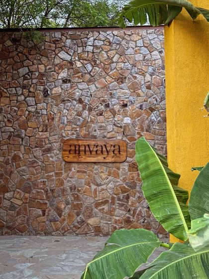 The Anvaya sign, carved in wood and set against a rustic stone wall, marks the entrance to your quiet escape.