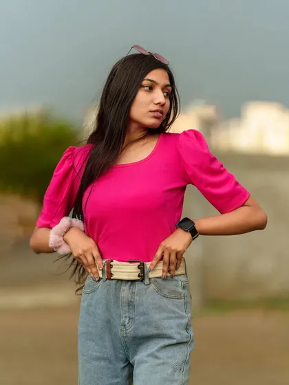 A close-up portrait focusing on the model's confident expression and the details of her pink top and belted jeans.
