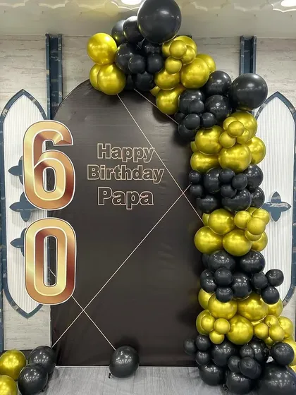We help you celebrate the most important people in your life. This sophisticated 60th birthday decoration for a client's father uses a classic black and gold color scheme with a personalized backdrop and a bold balloon garland.