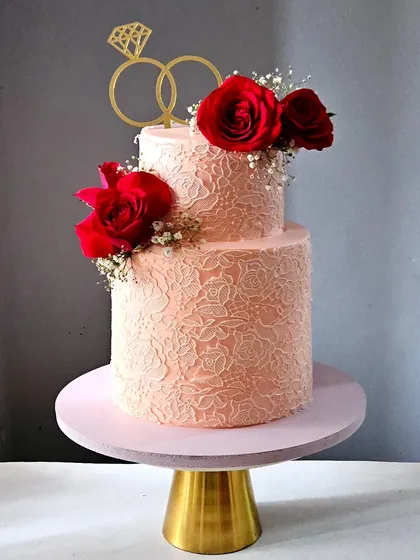 Elegance is in the details. This two-tiered engagement cake features an intricate, edible lace pattern wrapped around a smooth whipped cream finish, adorned with fresh red roses. It’s a design that is both classic and breathtaking.