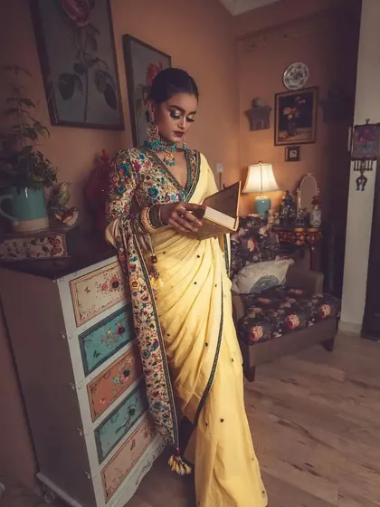 Creating a story through styling. In this shot, the model, dressed in the elegant yellow saree and embroidered blouse, interacts with the vintage-inspired set, adding a narrative quality to the fashion photograph.
