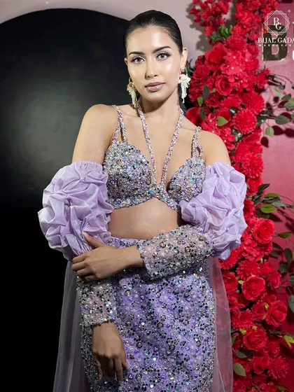 Posing against a vibrant red floral background, the lilac gown stands out beautifully. This shot highlights the contrast between the soft pastel dress and the bold backdrop.