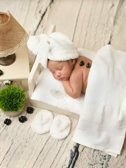 Welcome to the baby spa! This newborn is enjoying a 'hot stone' massage, complete with a towel wrap. This is a unique and humorous theme that parents love.