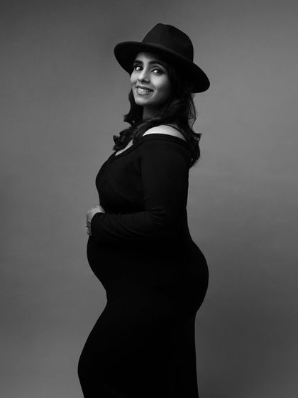 A stylish mom-to-be adds a hat to her classic black dress, creating a chic and modern monochrome portrait.