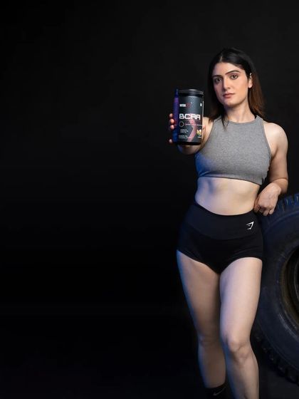 A medium shot with the model leaning against a prop tire, holding the BCAA product forward. The composition is balanced and uses negative space effectively, making it suitable for various digital marketing formats.
