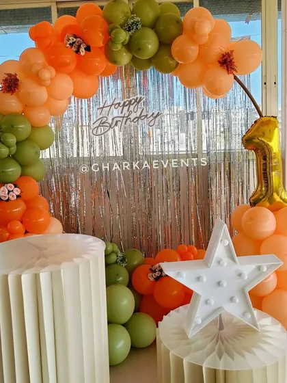 Another view of the orange and green balloon arch with a tinsel backdrop. The different textures and colors work together to create a visually interesting photo corner.
