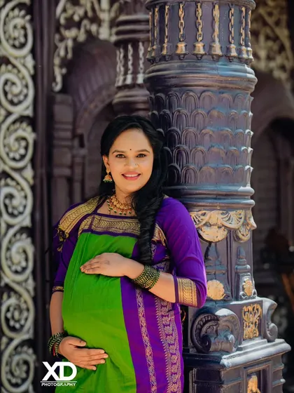 A joyful portrait of the mother-to-be, her bright smile lighting up the frame as she stands by a traditional pillar.