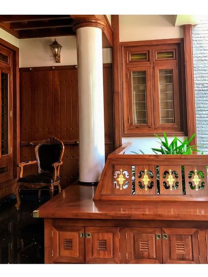 This elegant sit-out space, or verandah, showcases the beauty of traditional woodwork. The polished wood, classic furniture, and detailed joinery create a serene space for relaxation, typical of a Kerala veedu.